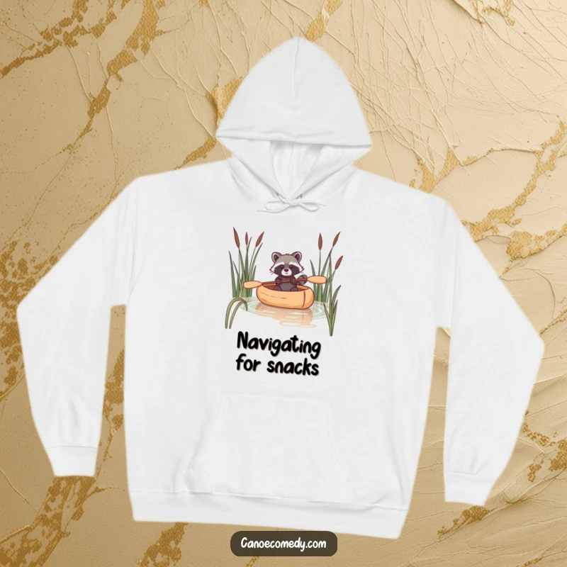 Funny raccoon hoodie depicting a raccoon navigating a canoe through reeds, perfect for staying warm and witty.