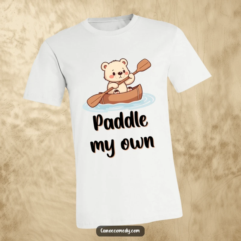 Funny t-shirt design of a small bear cub paddling a canoe with serious, determined effort.